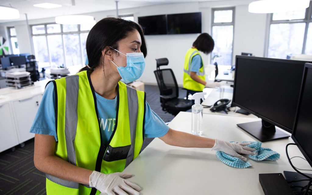 Woman wearing hi vis vest and face mask cleaning the office using disinfectant