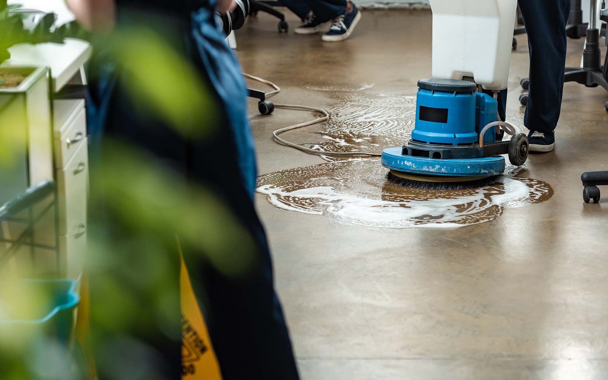 cropped view of cleaner washing floor with cleaning machine near colleagues